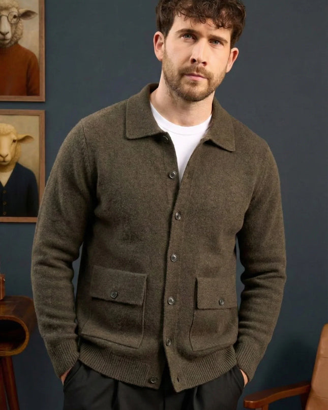 Man wearing a brown cardigan standing against a blue wall with framed pictures of sheep.
