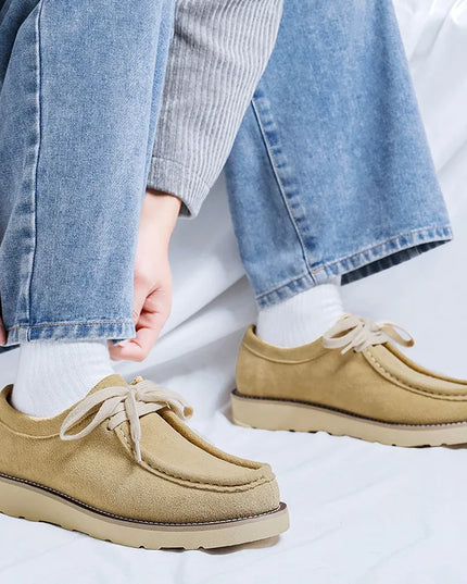 Beige loafers worn with blue jeans on a white background