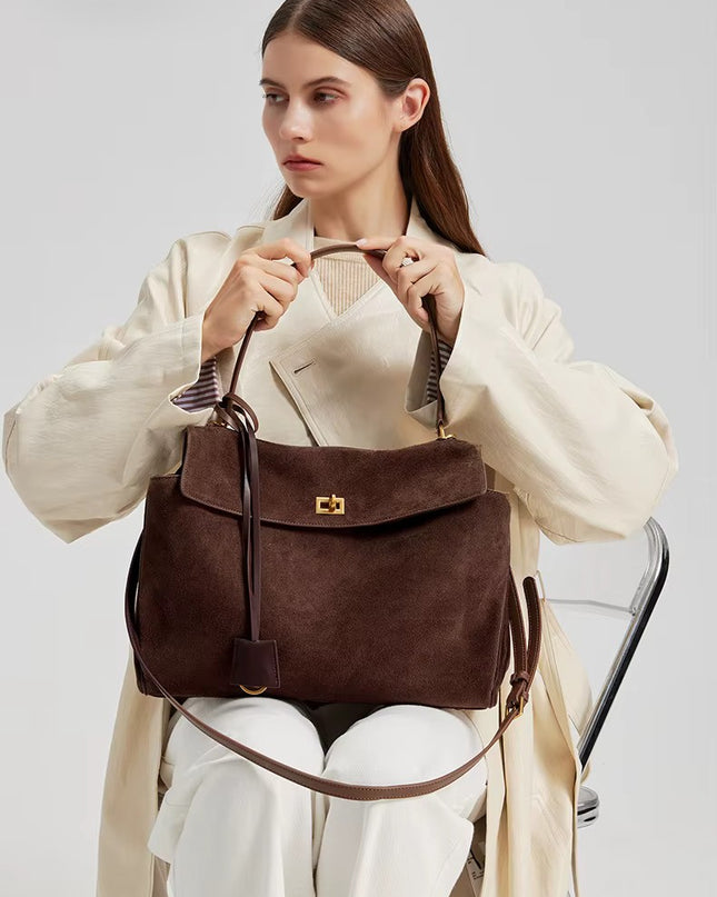 Woman holding a brown suede handbag against a plain background