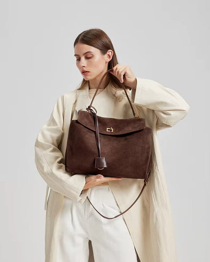 Woman holding a brown leather handbag against a plain background