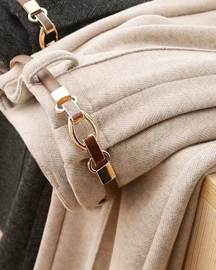 Close-up of a beige coat with a gold and brown strap on a wooden surface.