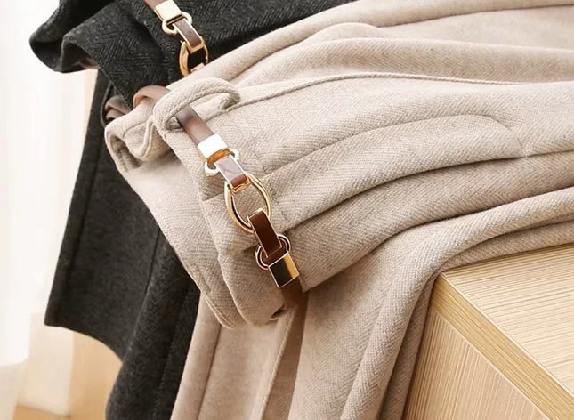 Close-up of a beige coat with a gold and brown strap on a wooden surface.