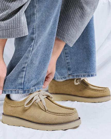 Beige shoes worn with blue jeans on a light gray background