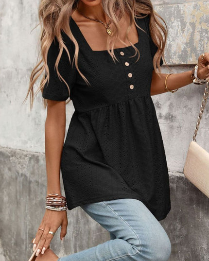 Woman wearing a black top with buttons and light blue jeans against a textured wall.