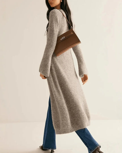 Woman wearing a long gray cardigan and blue jeans, holding a brown handbag on a beige background