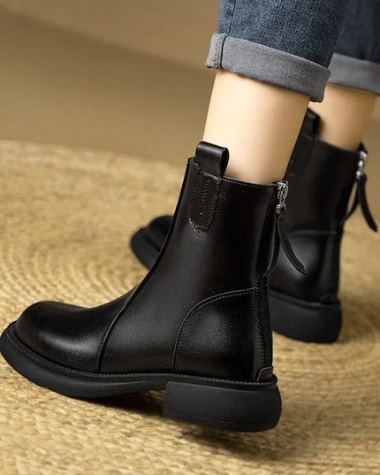 Black leather boots worn with rolled-up jeans on a textured surface