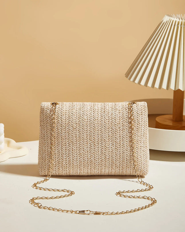 Beige woven handbag with a gold chain on a light surface with a beige wall and lamp in the background.
