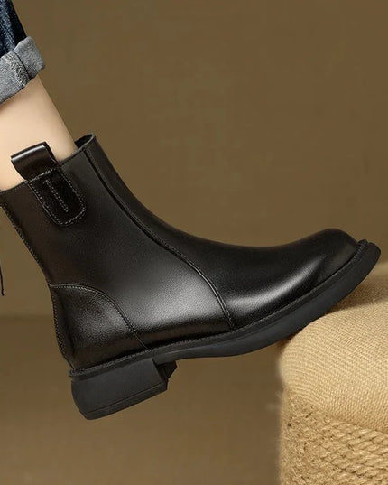 Black leather ankle boot with a zipper on a brown background