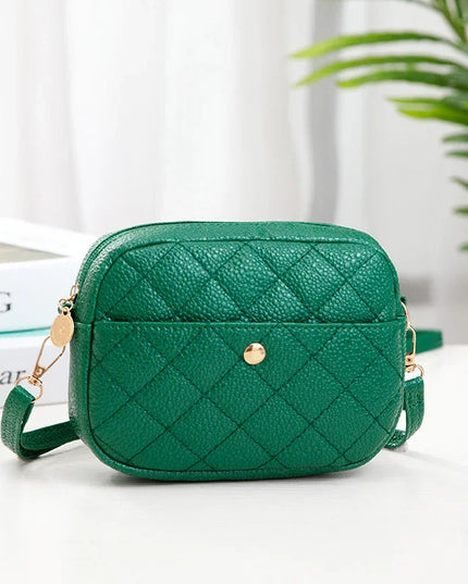 Green quilted handbag on a white surface with a plant in the background
