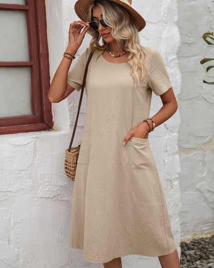 Woman wearing a beige dress and straw hat against a white stone wall.
