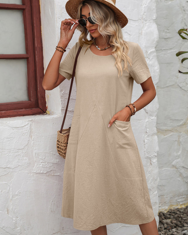 Woman wearing a beige dress and straw hat against a white stone wall.