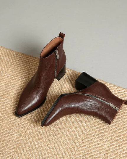 Pair of brown leather ankle boots with zippers on a textured surface.