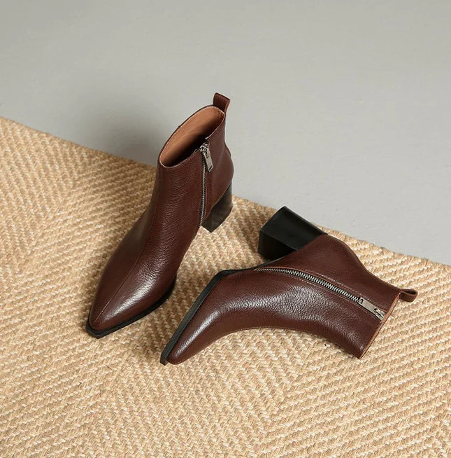 Pair of brown leather ankle boots with zippers on a textured surface.