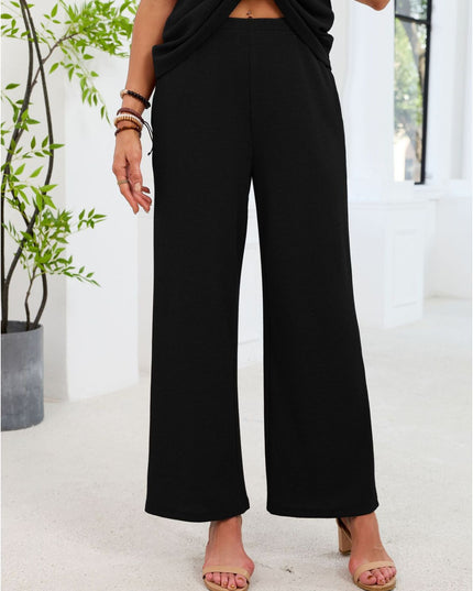 Person wearing black wide-leg pants standing indoors with a plant in the background