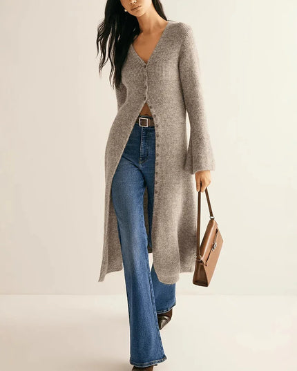 Woman wearing a long gray cardigan over a brown top, blue jeans, and holding a brown handbag on a beige background.