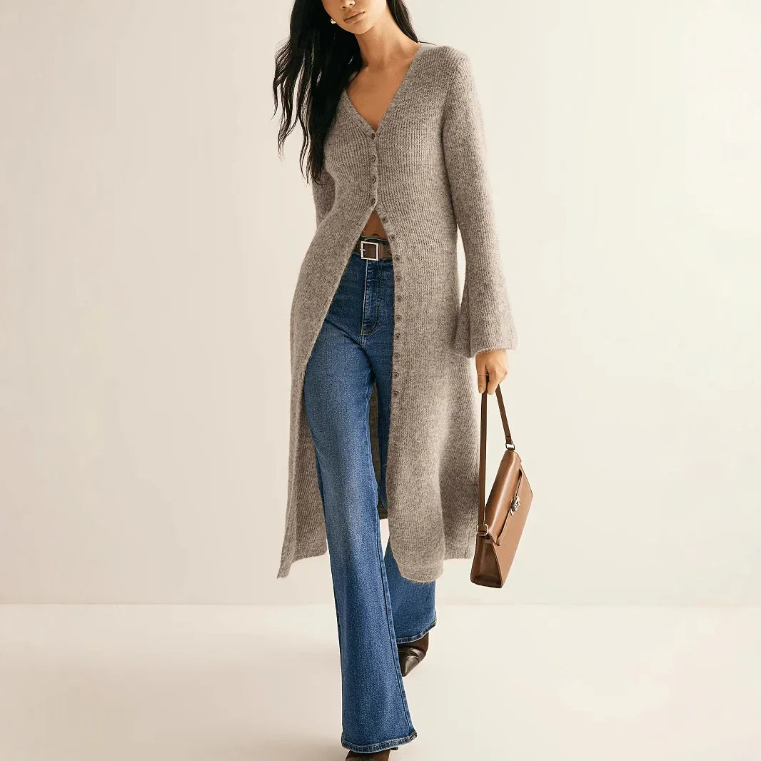 Woman wearing a long gray cardigan over a brown top, blue jeans, and holding a brown handbag on a beige background.