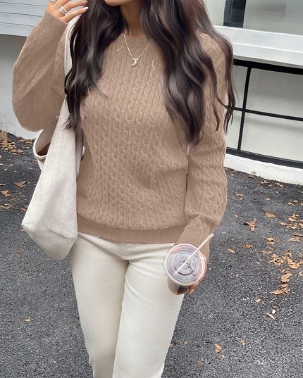 Person wearing a brown sweater and white pants, holding a drink, standing on a road with a building in the background.