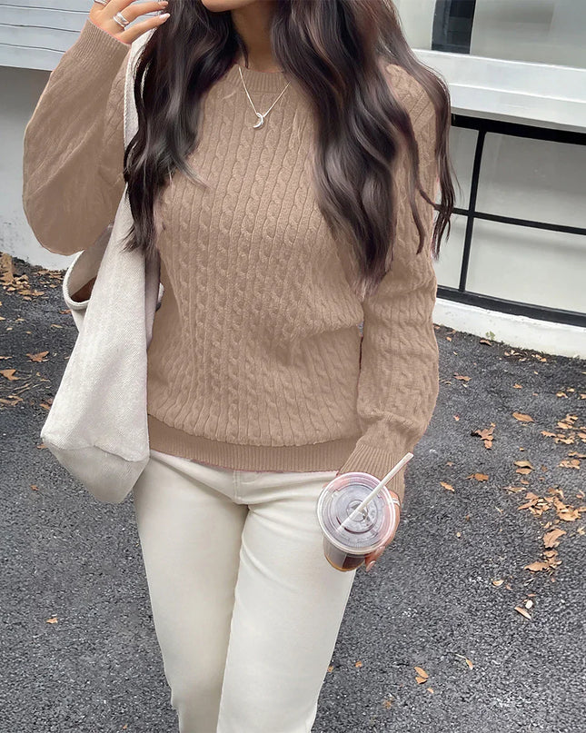 Person wearing a brown sweater and white pants, holding a drink, standing on a road with a building in the background.