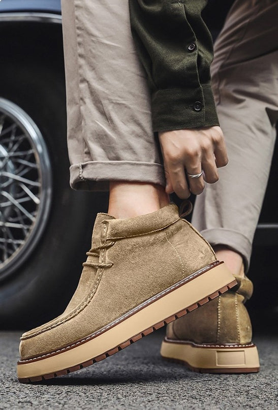 Person wearing brown suede boots with a car tire in the background