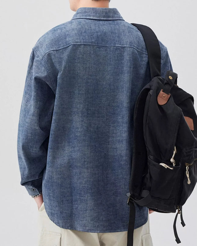 Person wearing a blue denim shirt and carrying a black backpack on a plain background