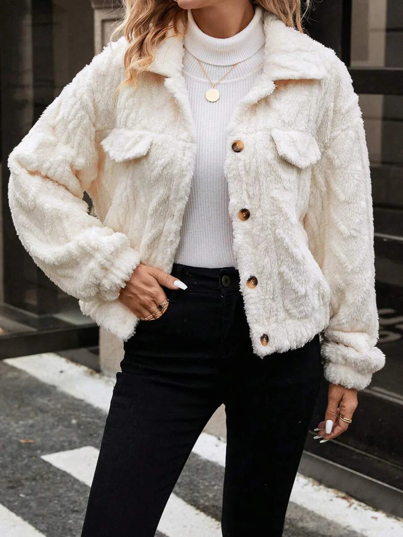 Person wearing a white fluffy jacket with brown buttons on a street.