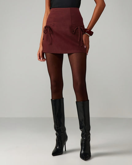 Person wearing a burgundy skirt and black knee-high boots on a gray background