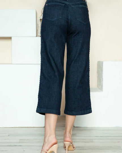 Dark blue jeans worn by a person on a light wooden floor.