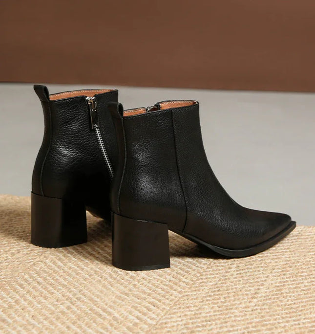 Pair of black leather ankle boots with block heels on a textured surface.