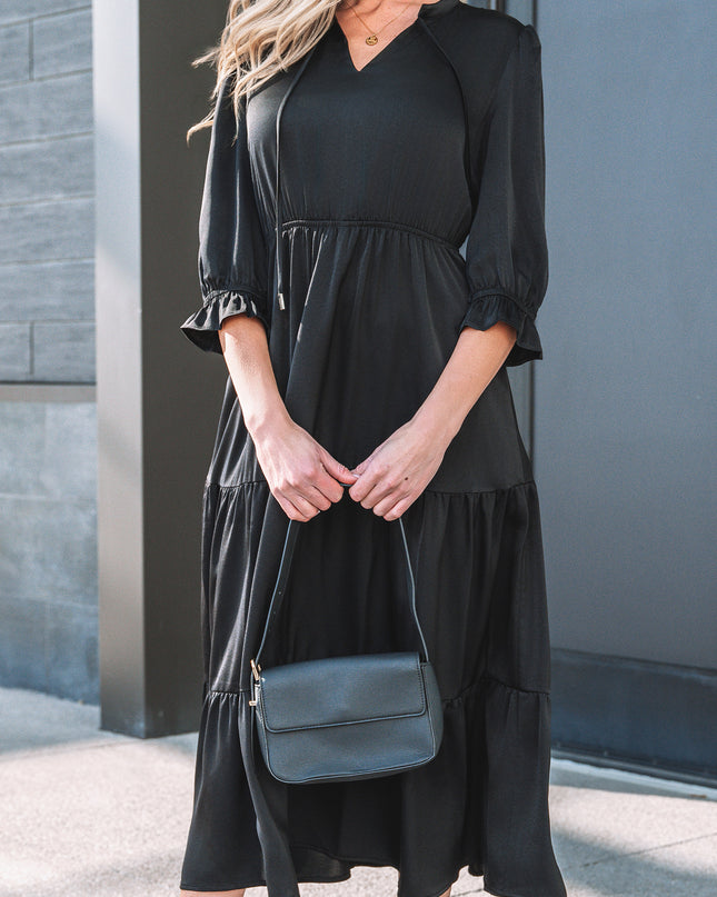 Woman wearing a black dress holding a blue handbag against a gray wall.