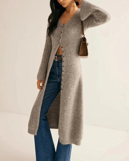 Woman wearing a long gray cardigan and blue jeans on a plain background