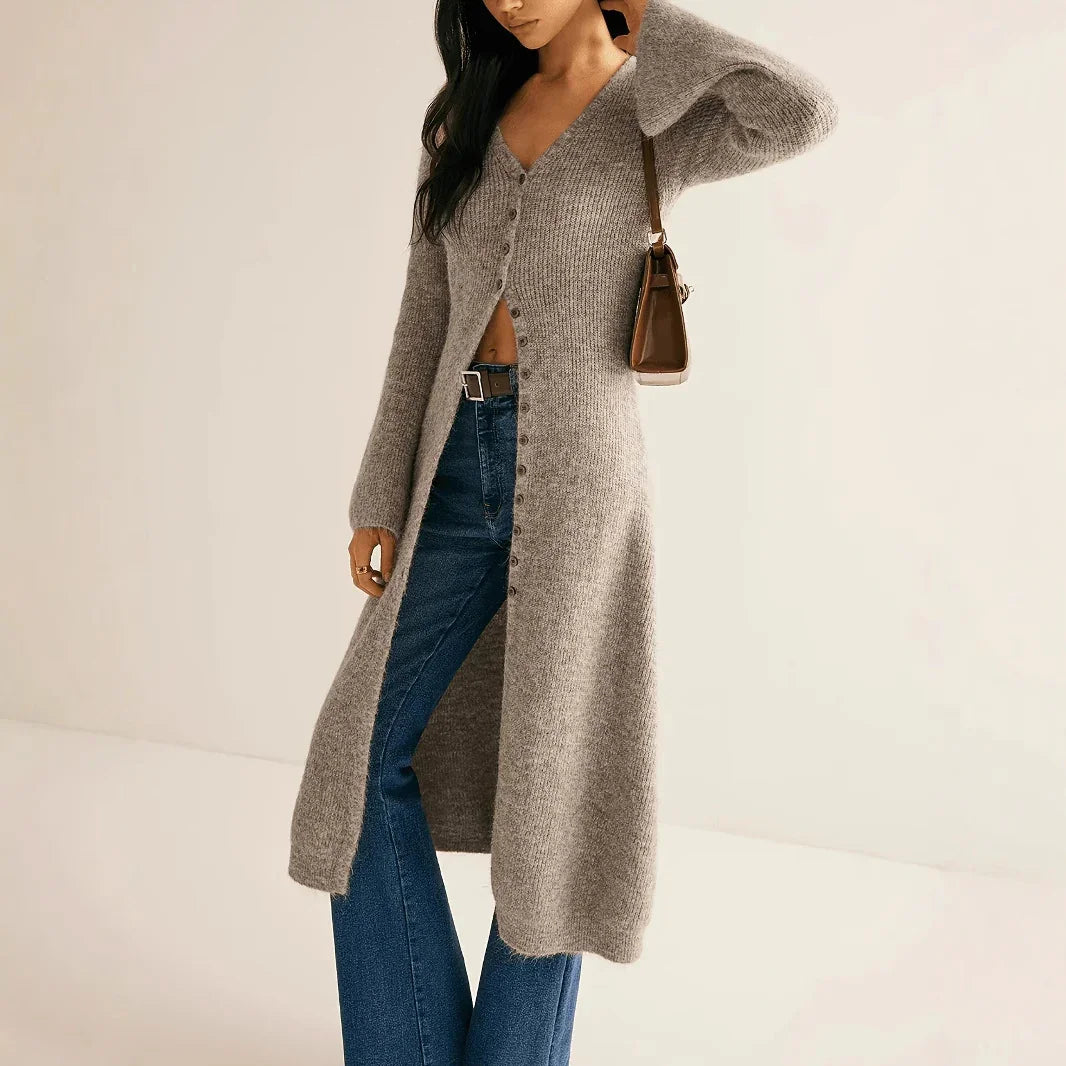 Woman wearing a long gray cardigan and blue jeans on a plain background