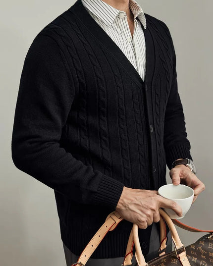 Person wearing a dark cable knit cardigan holding a cup and a handbag against a neutral background