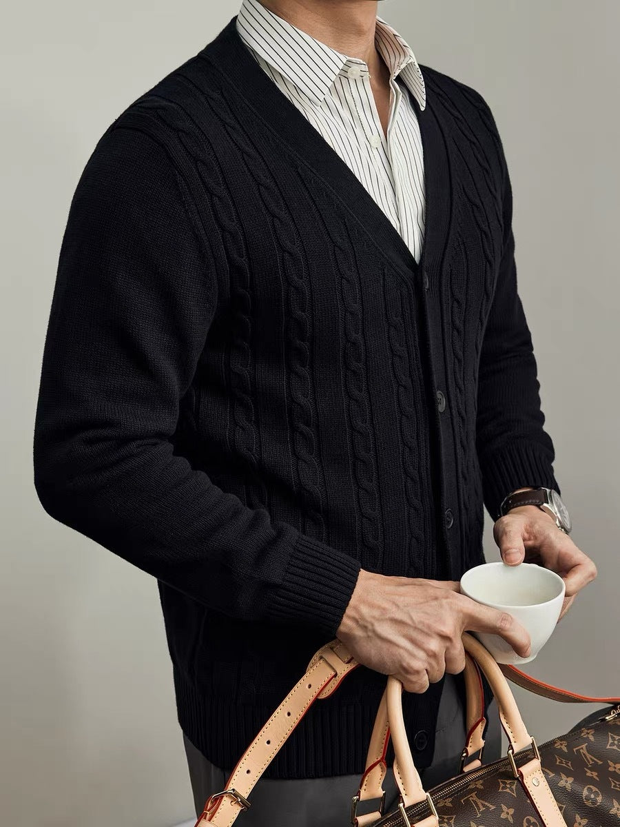 Person wearing a dark cable knit cardigan holding a cup and a handbag against a neutral background