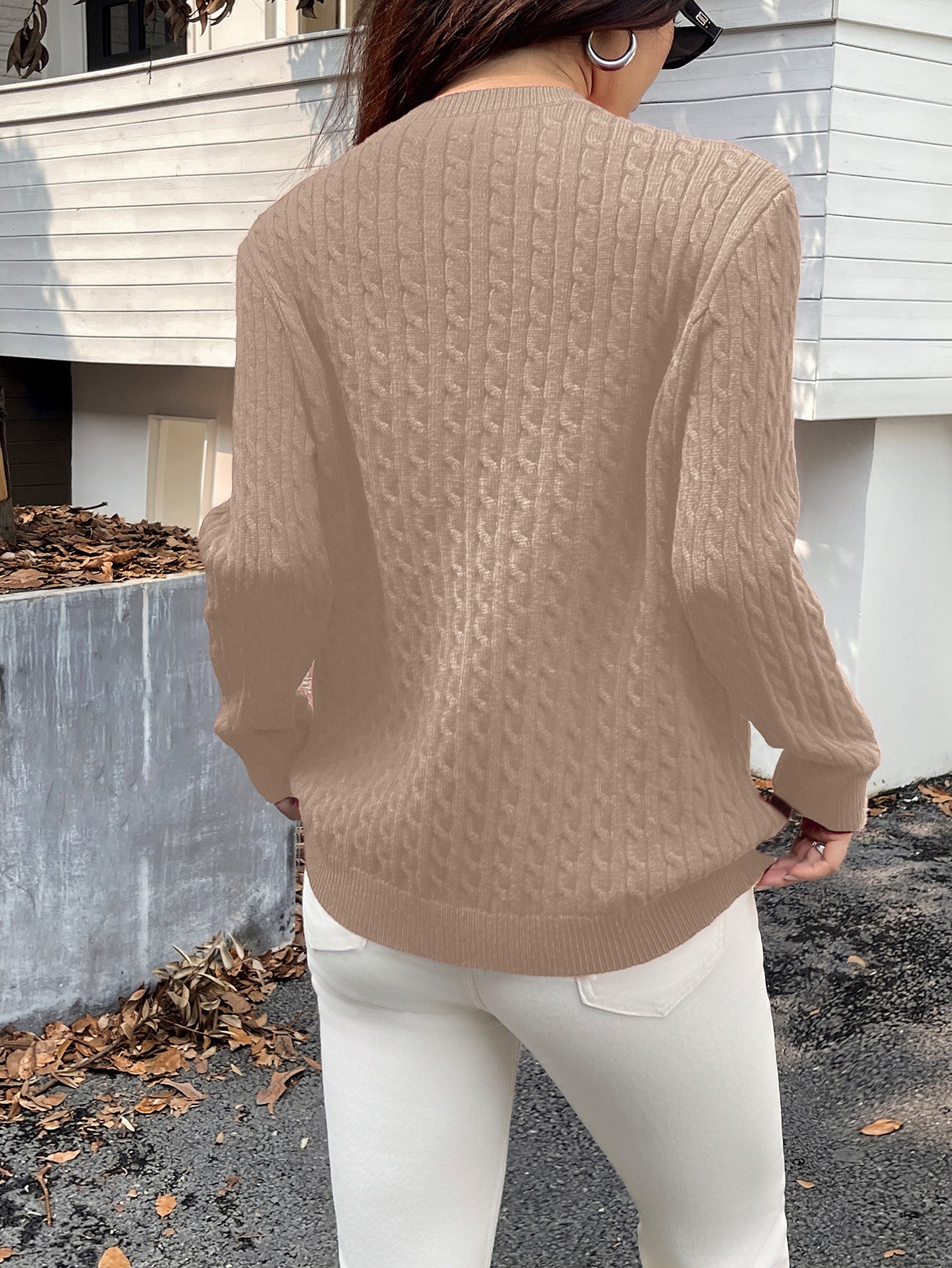 Person wearing a beige sweater and white pants standing outdoors.