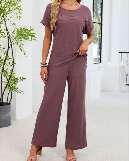 Woman wearing a mauve jumpsuit standing in a bright room with a plant.