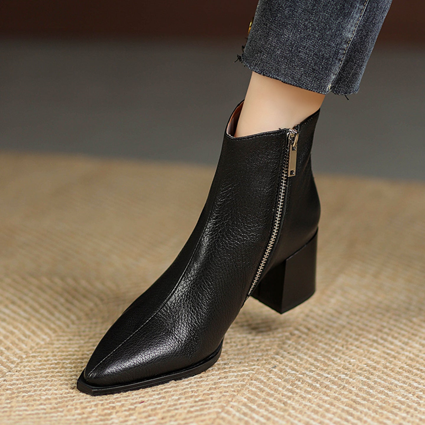 Black leather ankle boot with a zipper on a textured surface