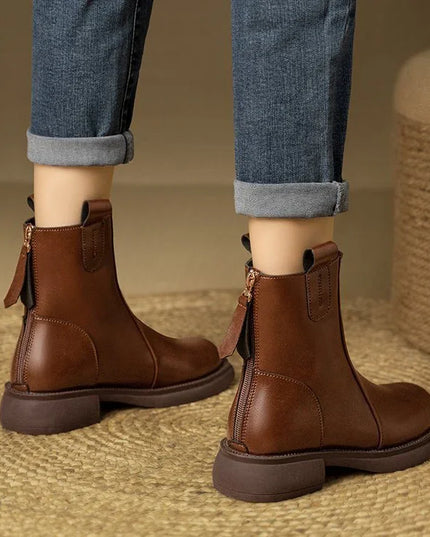 Brown leather boots worn with rolled-up jeans on a textured surface