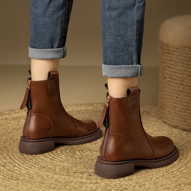 Brown leather boots worn with rolled-up jeans on a textured surface