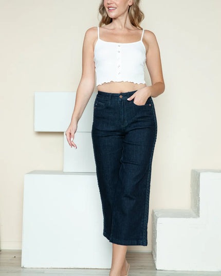 Woman wearing a white top and dark blue jeans standing against a light background