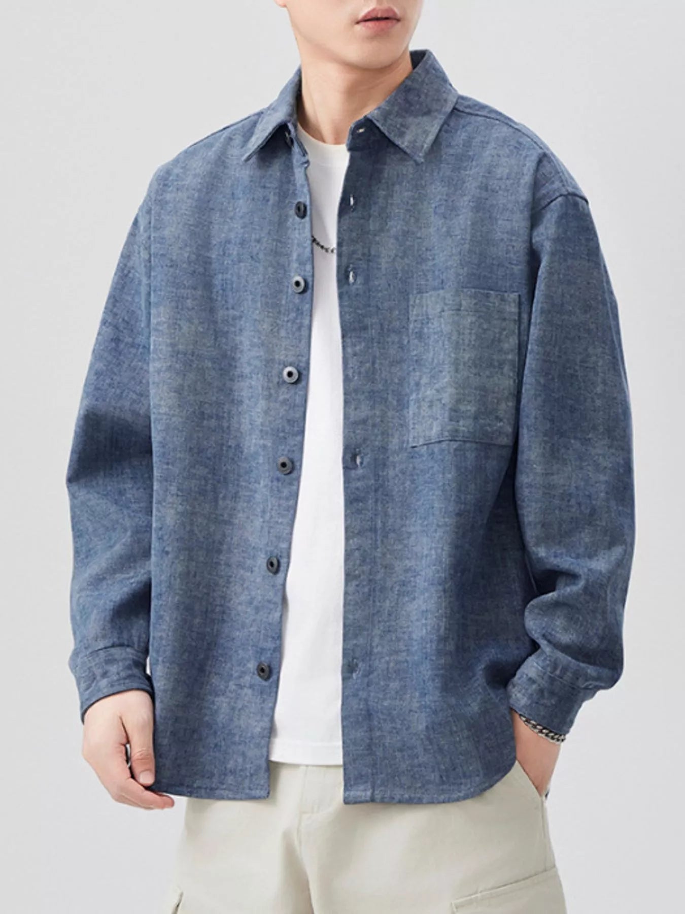 Person wearing a blue denim shirt over a white t-shirt on a light gray background