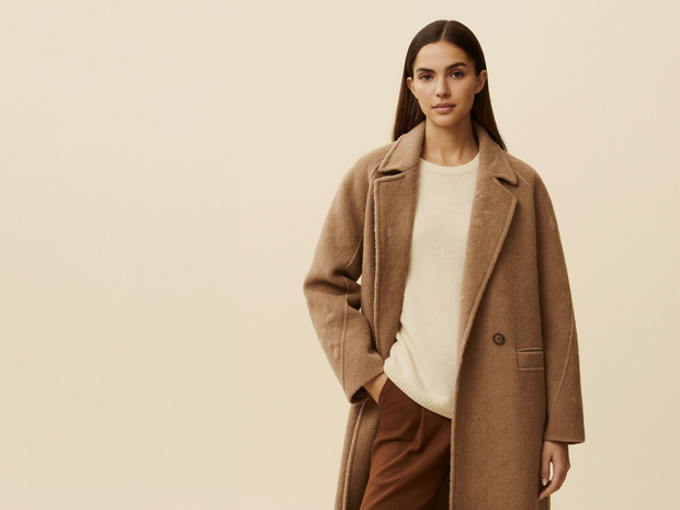 Woman in a long camel wool coat over a cream knit sweater