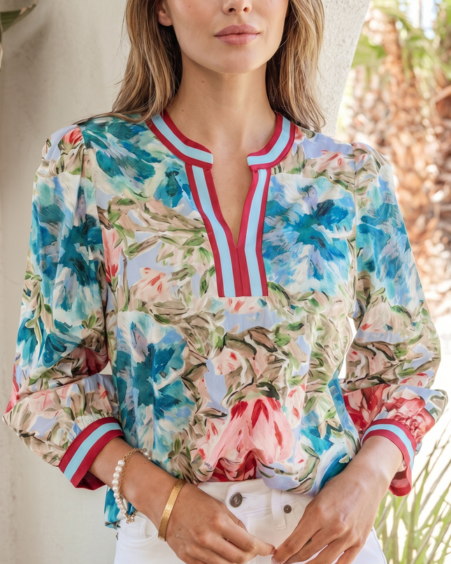 Woman wearing a colorful floral blouse with white pants outdoors.